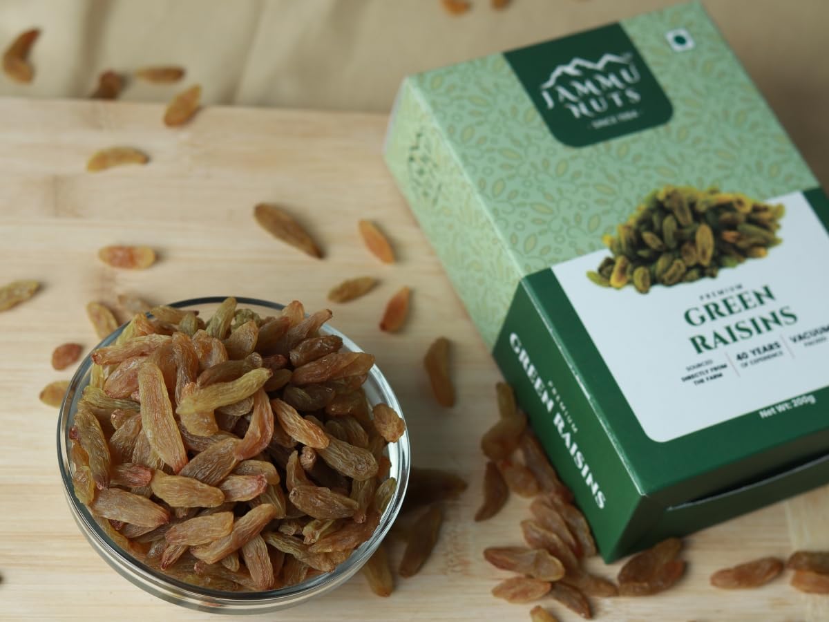 Green box of Jammu Nuts Green Raisins with a bowl of raisins on a wooden surface.
