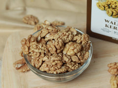 Glass bowl filled with walnuts on a wooden surface with a box labeled 'Walnut Kernel' in the background.